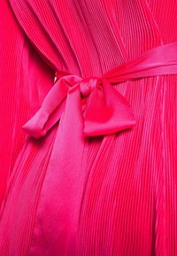 Robe plissée en tissu rose vif avec une texture lisse. Présente une ceinture nouée à la taille et des plis verticaux pour plus de dimension.