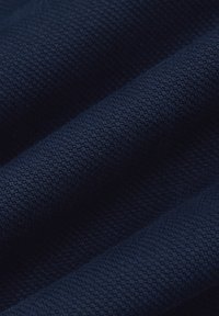 Ciemnoniebieska fakturowana tkanina z wplecionym wzorem, który tworzy delikatny efekt łusek, podkreślony miękkimi fałdami i cieniami.