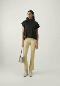 Top preto de manga curta combinado com calças texturizadas amarelas claras e botas de tornozelo bege; segurando uma pequena mala cinza clara.