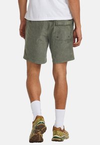 Groene katoenen shorts met een relaxed fit, voorzien van zijzakken en een achterzak met klep, gedragen met bruine sneakers en witte sokken.