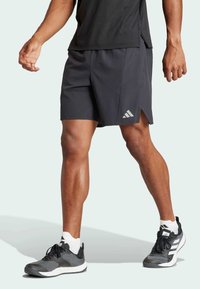 Svart träningsshorts med sidoslitsar, med en vit Adidas-logotyp. Kombineras med svarta och grå sneakers samt vita sportstrumpor.