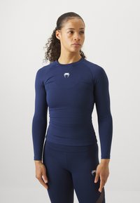 Tricou sportiv cu mânecă lungă de culoare bleumarin, cu un design ajustat, textură fină și logo alb pe piept. Asociați-l cu colanți bleumarin asortați.