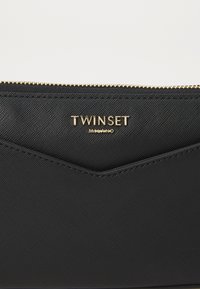 Black fabric clutch with a textured surface, gold zipper, and TWINSET branding in gold. Features a chevron design at the top.