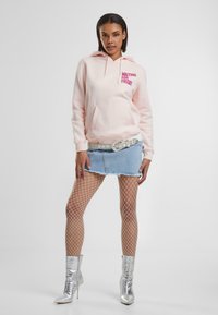 Helle rosa Kapuzenjacke mit dem Aufdruck "WAITING FOR FRIDAY" in fettem Pink, kombiniert mit einem Denim-Minirock und silbernen Ankle-Boots. Mit Netzstrumpfhosen.