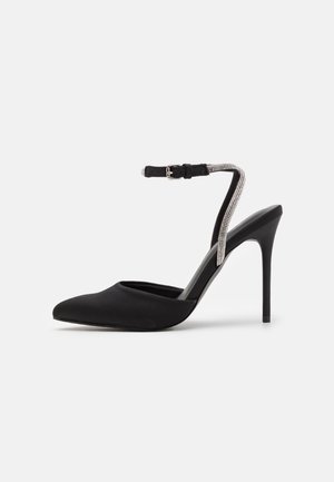 Schwarzer Slingback mit hohen Absätzen, gefertigt aus glattem synthetischen Material. Verfügt über eine spitze Zehenpartie und einen Knöchelriemen mit Strassakzenten.