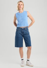 Light blue sleeveless knitted top with a button front, paired with dark denim knee-length shorts and white sneakers with black stripes.