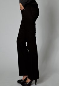 Musta denimiä oleva levenevä housu, jossa on korkeavyötärö, sivutaskut ja sileä pinta, yhdistettynä mustiin korkeakorkoisiin kenkiin.