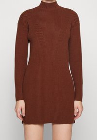 Braunes, geripptes Strickkleid mit hohem Kragen, langen Ärmeln, figurbetontem Schnitt und seitlichen Schlitzen am Saum für mehr Bewegungsfreiheit.