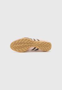 Rosa sneaker sål med sorte striber og en tekstureret gummibund. Har et bølge mønster for greb og stabilitet.