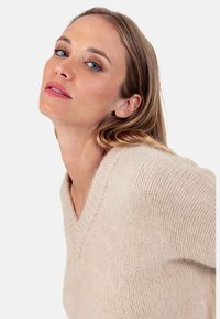 Strickpullover mit V-Ausschnitt in Hellbeige, aus weichem, strukturiertem Stoff, mit lockerem Schnitt und gerippten Details am Halsausschnitt.