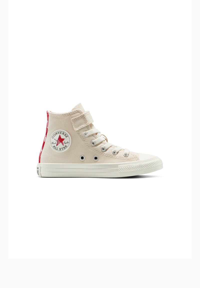 Beige hoge sneakers van canvas materiaal, met klittenbandsluiting, witte rubberen neuskap en rode accenten op de hiel. Heeft een logo-opdruk aan de zijkant.