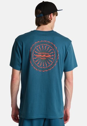 Türkises Baumwoll-T-Shirt mit einem kreisförmigen Motiv mit roten Wellen und Text auf der Rückseite sowie kurzen Ärmeln. Ergänzt legere Kleidung.