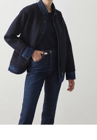 Marinblå jacka med denimdetaljer, med dragkedja framtill och tryckknappar. Kombinerad med högmidjade mörka jeans av denim som visar subtil textur.