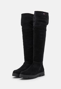 Stivali sopra il ginocchio in suede nero con superficie texturizzata, suola in gomma e un leggero plateau. Presentano un colletto piegato nella parte superiore.