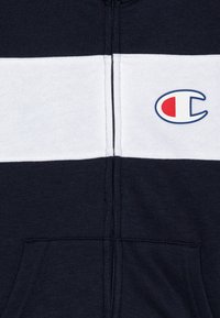 Champion zip-up hoodie in navy en wit. Heeft een voorzak, zachte stof en geborduurd logo op de linkerborst.