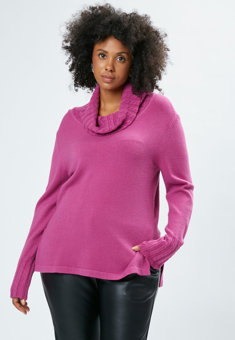 Magenta sweater med hætte og ribbede detaljer på ærmerne, afslappet pasform og sideslidser, parret med sorte slim-fit bukser.