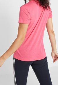 Camiseta rosa de manga corta hecha de tela ligera, con cuello redondo y silueta ajustada, combinada con leggings oscuros.