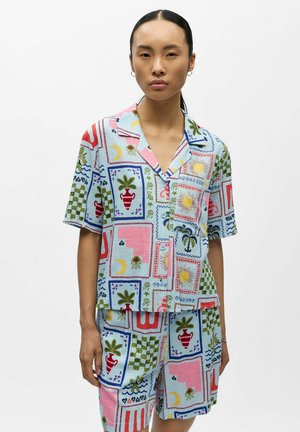 Joven mujer vistiendo una camisa de manga corta y pantalones cortos a juego en tonos pastel, con patrones abstractos coloridos y motivos de la naturaleza.