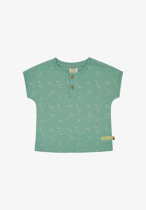 Camicia verde di cotone a maniche corte con piccoli motivi di uccelli beige, due bottoni in legno al collo e un'etichetta colorata sull'orlo laterale.