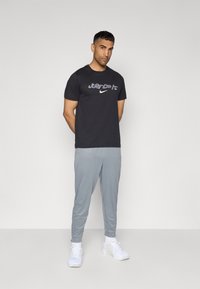Sort bomulds T-shirt med "JUST DO IT." grafik og Nike-logo, parret med lysegrå tapered joggers og hvide sportsko.