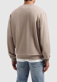 Lichtbeige sweatshirt met lange mouwen, geribde manchetten en onderrand. Glad stoftextuur en een subtiele logodetail net onder de halslijn op de rug.