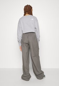 Šedá mikina s bílým logem na horní zadní straně, v kombinaci s volně střiženými šedými kalhotami, které mají elastický pas a zúžené nohavice.