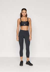 Bustier sport negru cu bretele ajustabile, asortat cu colanți negri cu talie înaltă și pantofi sport negri. Material neted și elastic pe toată suprafața.