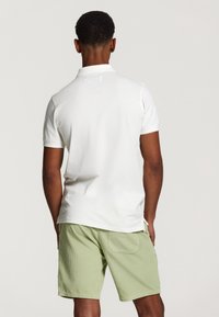 Polo shirt blanc à manches courtes avec une texture douce, associé à un short en velours côtelé vert clair doté d'une poche arrière et d'un style décontracté.