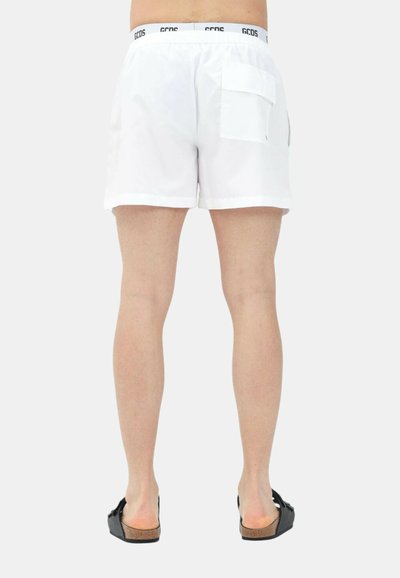 Hvide shorts lavet af letvægtsstof, med en elastisk talje med logo og en baglomme. Båret med sorte sandaler.
