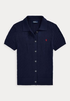 Tmavomodrý krátky kardigán s krátkym rukávom, textúrou z pletenia s vrkočmi, zapínaním na gombíky, golierom a malým červeným vyšívaným logom na ľavej strane hrudníka.