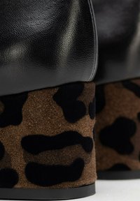 Scarpa di pelle nera con tacco in suede marrone caratterizzata da un motivo a stampa leopardo nero. Texture liscia sulla parte superiore; tacco morbido e testurizzato.