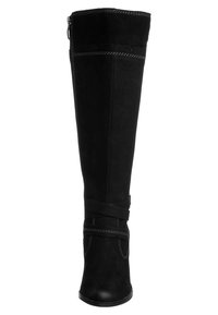 Bota de ante negra hasta la rodilla con un acabado suave, costuras decorativas y una correa ajustable cerca del tobillo. Punta redonda y tacón bajo.
