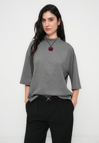 Γκρι φαρδύ t-shirt με ψηλό λαιμό και κοντά μανίκια, συνδυασμένο με μαύρο παντελόνι ψηλόμεσο και ζώνη με χρυσές λεπτομέρειες.