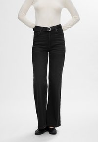 Črne jeans hlače ravnega kroja z visokim pasom, obdarjene s črnim pasom s srebrno sponko. Gladek, trpežen jeans material z minimalnimi šivi.