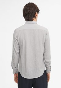 Camisa de manga larga de textura gris con cuello abotonado, detalles en la parte trasera y botones en los puños. Tejido suave y tejido con un patrón sutil.