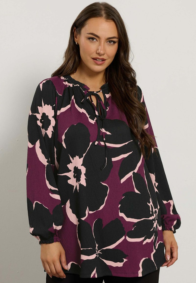 Blusa a maniche lunghe con scollatura arricciata e dettagli con fiocco. Base viola scuro con grandi motivi floreali neri e rosa; tessuto testurizzato.