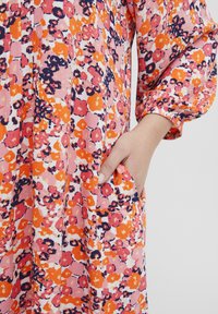 Rochie cu imprimeu floral colorat, având nuanțe de roz, portocaliu și bleumarin. Croială lejeră, cu mâneci lungi și buzunare. Material moale și ușor.