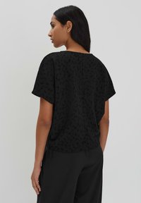 Zwart T-shirt met korte mouwen en een gestructureerd patroon, met een ontspannen pasvorm en een ronde halslijn, gecombineerd met zwarte broek.