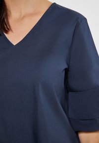 Navyblaue Bluse mit V-Ausschnitt, kurzen Rüschensleeves und glattem, leichtem Stoff mit einem dezenten Glanz.