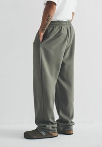 Grüne, lässige Sweatpants mit einem elastischen Bund, seitlichen Taschen und einer weichen Textur, kombiniert mit braunen Clogs mit einer Metall-Schnalle.