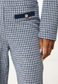 Geweven stoffen broek met een blauw-wit ruitpatroon. Bevat een marineblauwe accentzak en een gestructureerde afwerking. Ronde gouden knoopdetail.