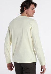 Long-sleeve, light yellow T-shirt in cotton, featuring a relaxed fit, round neckline, and cuffed sleeves. Minimalist design, no visible logos.