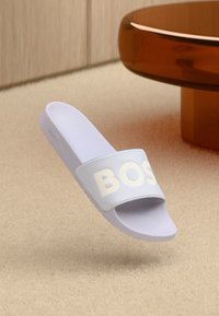 Ανοιχτό μοβ σανδάλι με πλατιά λουρί που φέρει τη λέξη "BOSS" σε λευκό, κατασκευασμένο από εύκαμπτο υλικό, με υφασμένο πάτο.