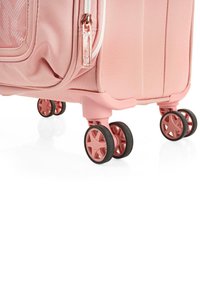 Equipaje de color rosa claro con una superficie texturizada, que cuenta con un zipper plateado y cuatro ruedas multidireccionales negras con acentos rosas.