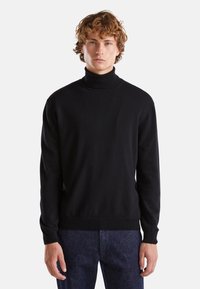 Maglione a collo alto di colore nero realizzato in un morbido tessuto a maglia fine. Presenta maniche lunghe e un ponte aderente, abbinato a pantaloni in denim scuro.
