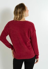 Pull rouge en peluche avec une coupe décontractée, un grand col et des poignets côtelés. Tissu doux et couleur unie sans motifs ni accents.