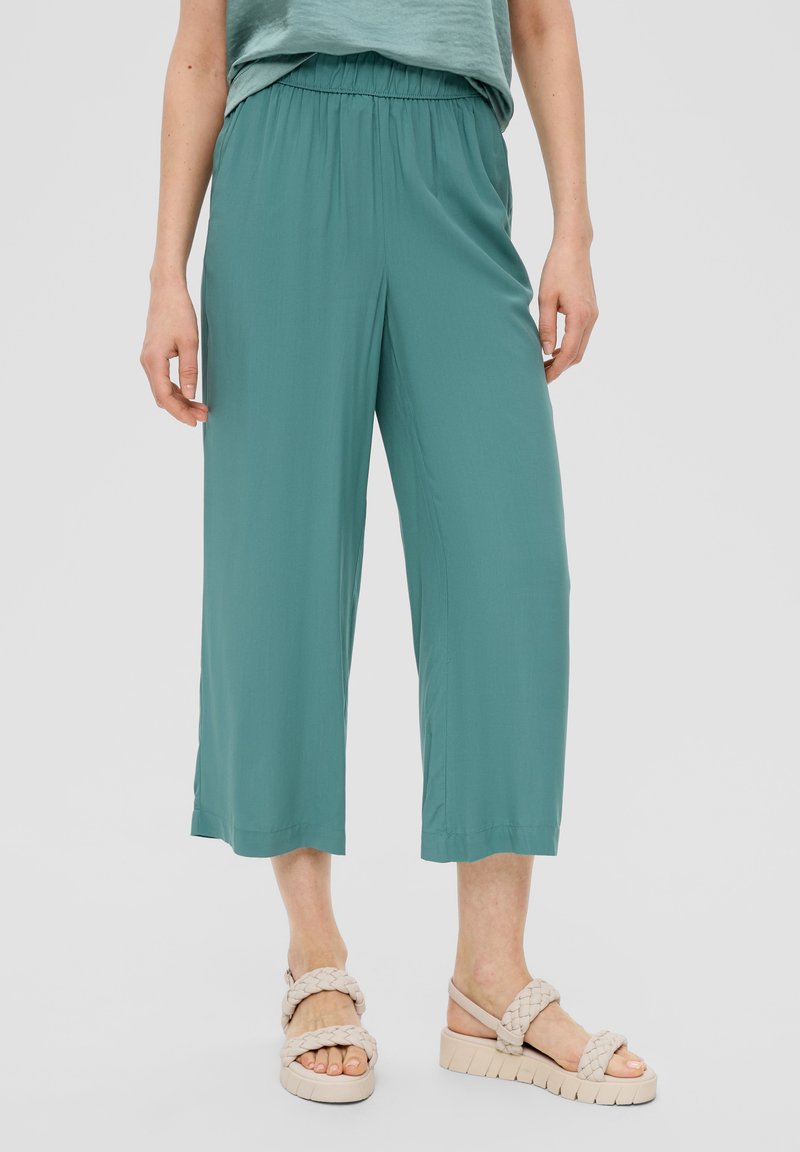 Teal wijde broek van lichtgewicht stof, met een elastische tailleband en rechte zoom. Gaat gepaard met beige gevlochten sandalen.