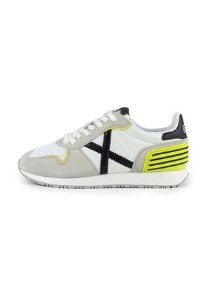 Zapatilla gris y blanca que presenta ante y malla, diseño de cruz negro, acentos en amarillo neón y una suela de goma texturizada.