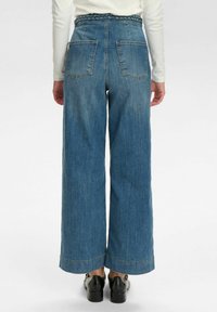 Vida jeans i ljusblå denim med vida ben, featuring en flätad midja och två bakfickor, samt sömnadsdetaljer vid fållen.