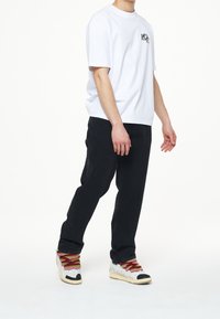 Vit kortärmad t-shirt med logotyp, kombinerad med svarta raka jeans och flerfärgade snörskor med en texturerad ovandel.